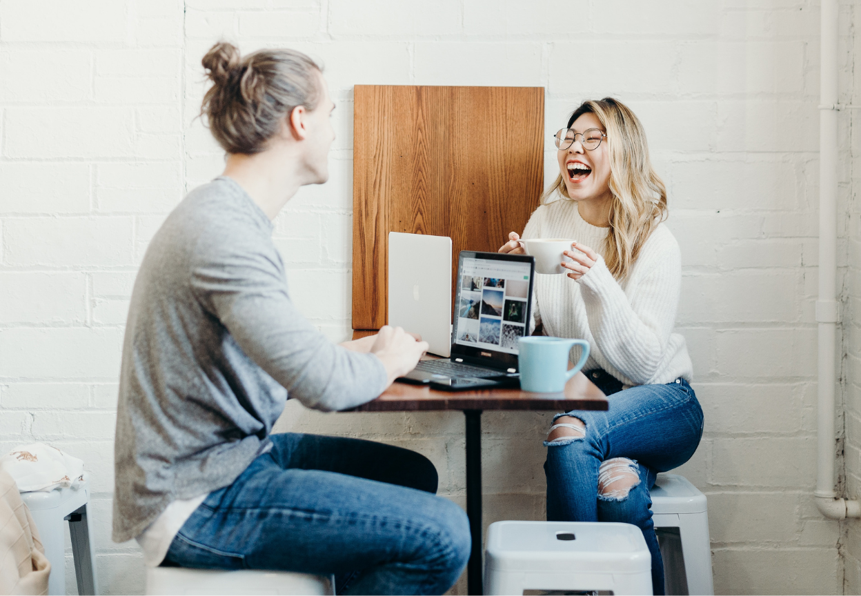 Kobieta i mężczyzna śmieją się siedząc przy komputerach